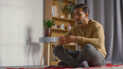 Muslim-Man-Praying-Holding-Prayer-Beads-Sitting-On-Floor-At-Home
